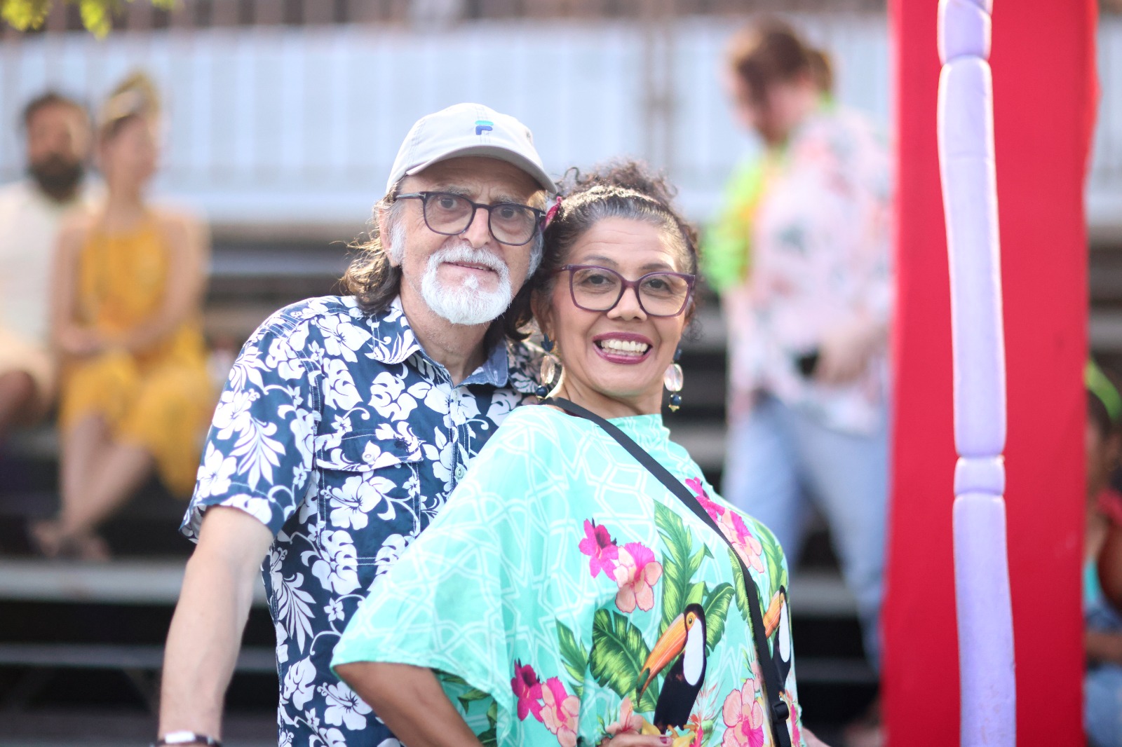 Claude e Walquiria. ele veste camisa estampada com tom predominantemente azul e ela veste blusa verde com estampa floral